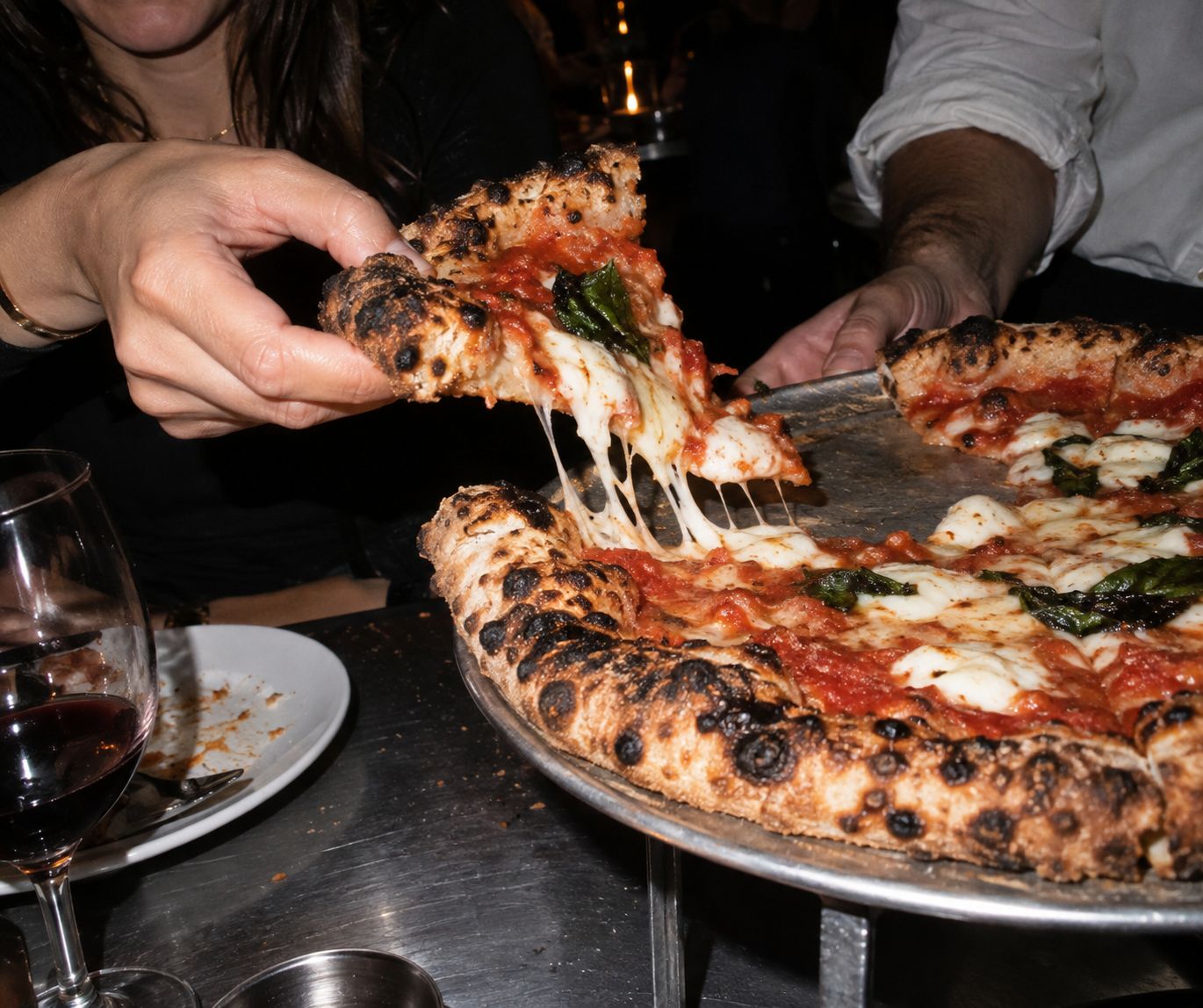 A slice of margherita lifted from the tray, mozzarella stretching